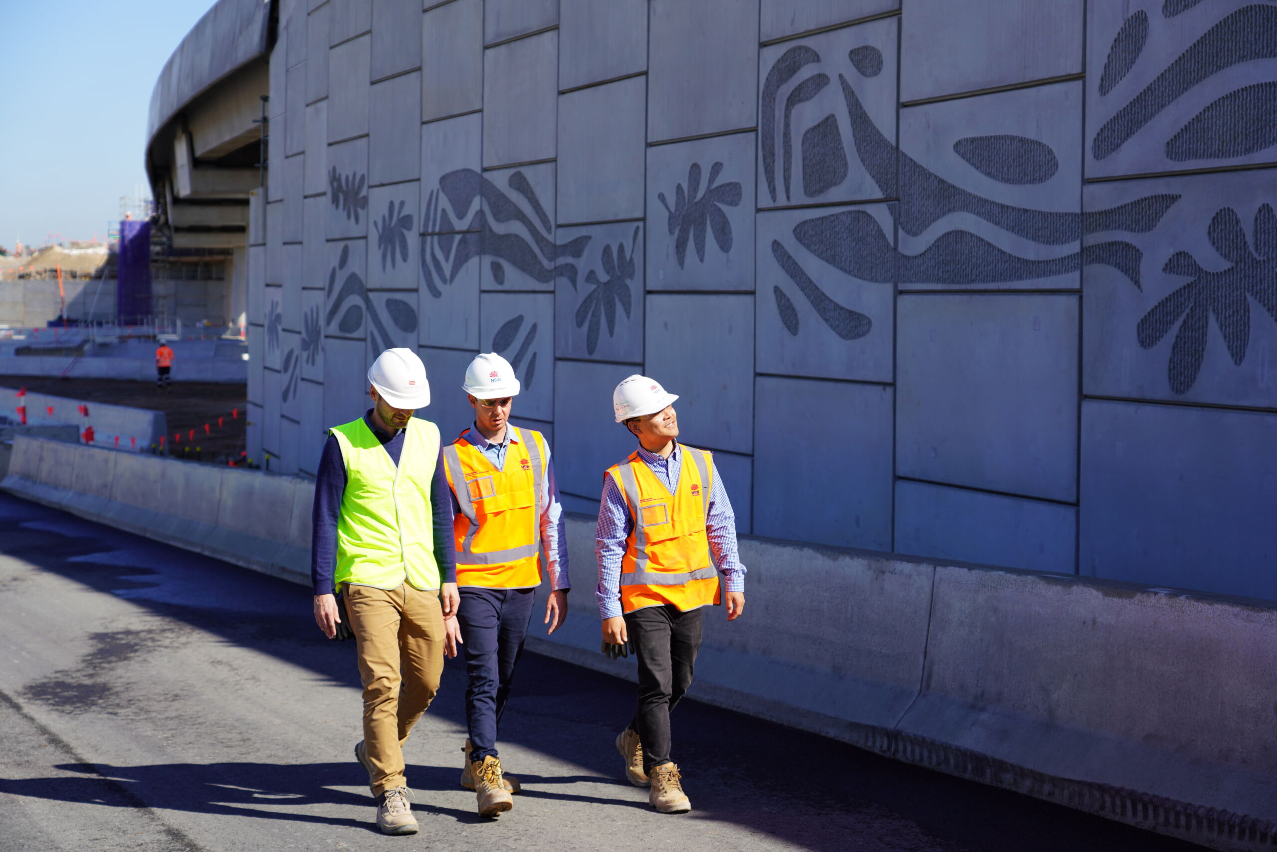 Engineers inspecting a completed reinforced earth wall (MSE wall) in Sydney, New South Wales, which has pre cast concrete facing panels with decorative elements engraved.