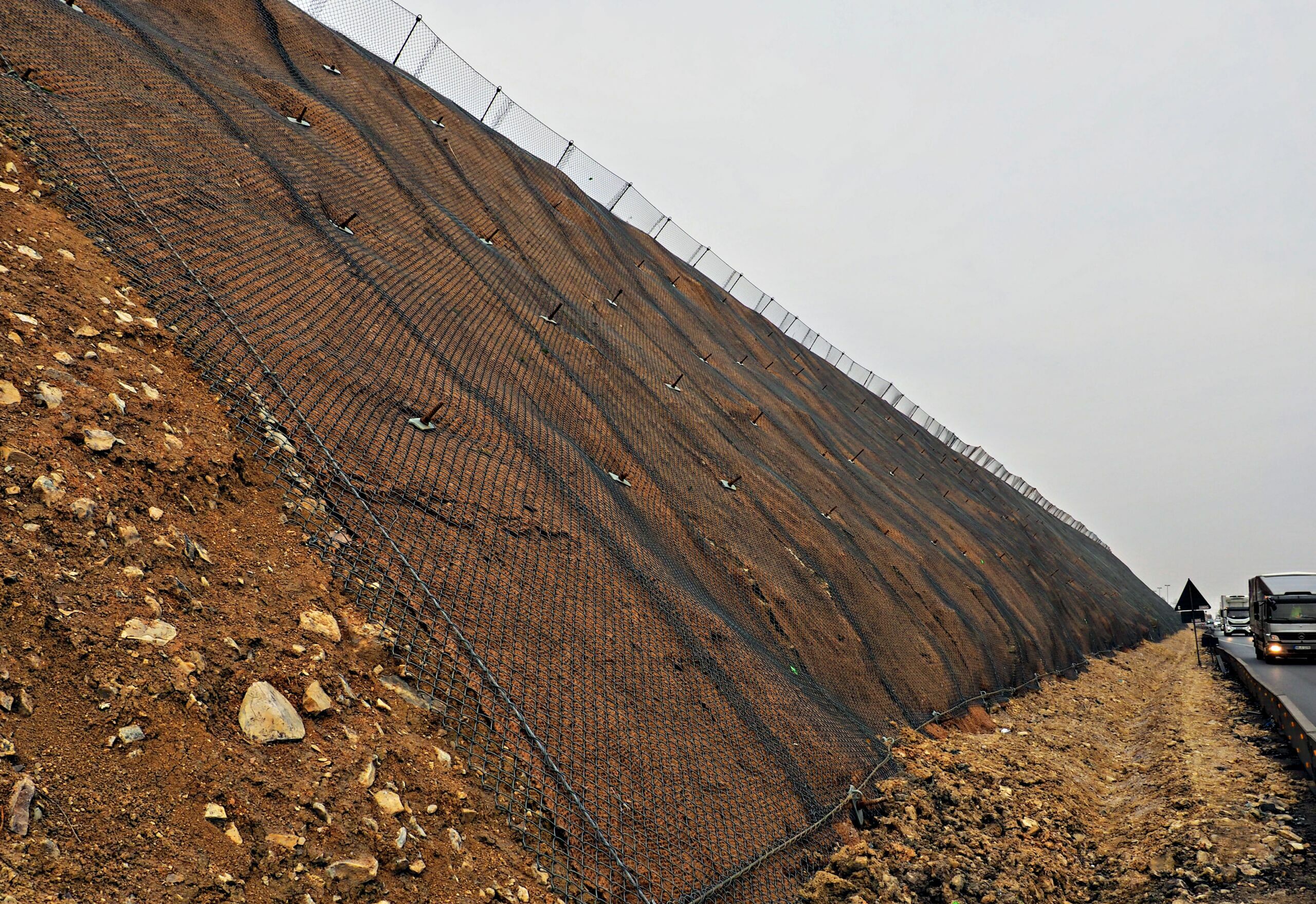 Geotechnical slope stablisation net ictured on a steep slope. Slope remediation and soil stablisation techniques include drainage, soil reinforcement, nets and erosion control matting.