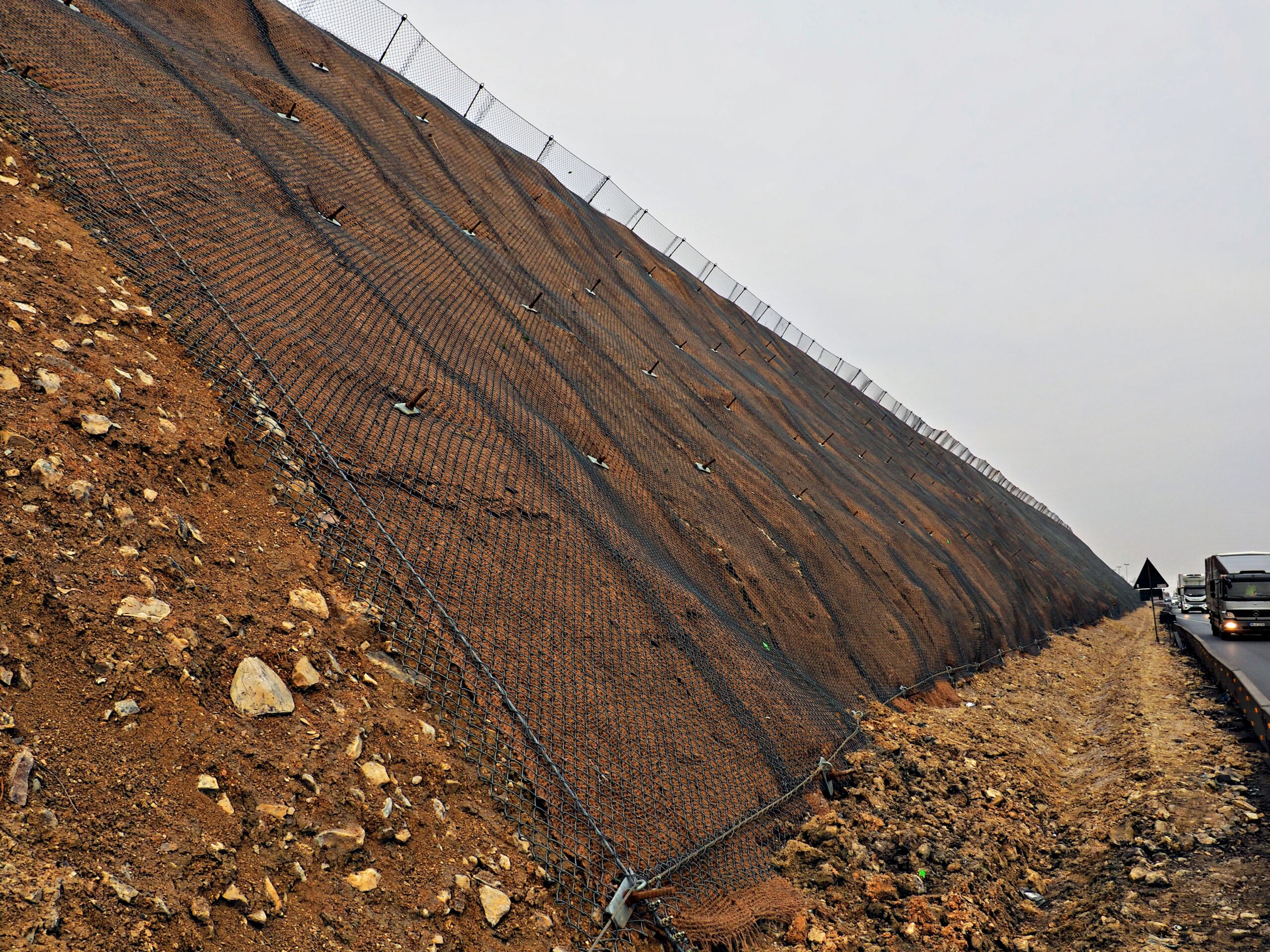 Geotechnical slope stablisation net ictured on a steep slope. Slope remediation and soil stablisation techniques include drainage, soil reinforcement, nets and erosion control matting.